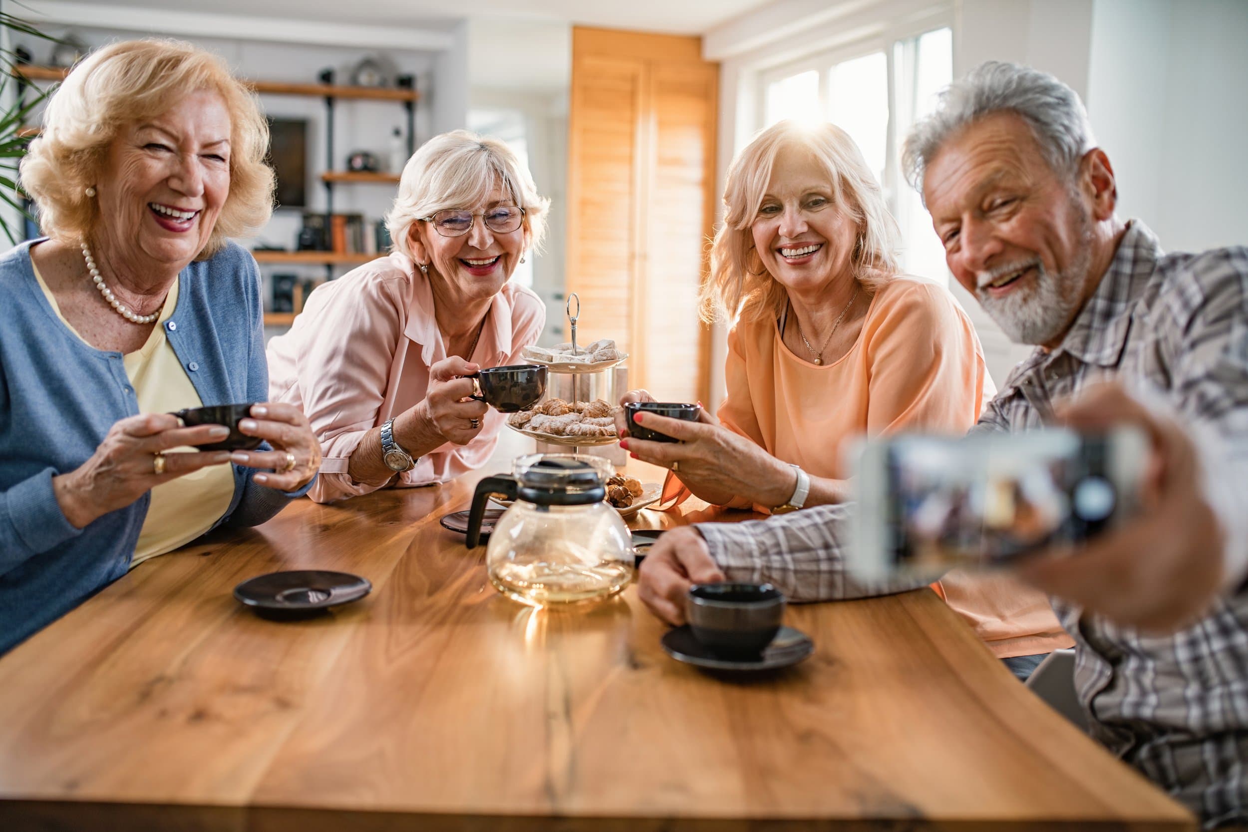A group of older friends laughing together while taking a selfie at home